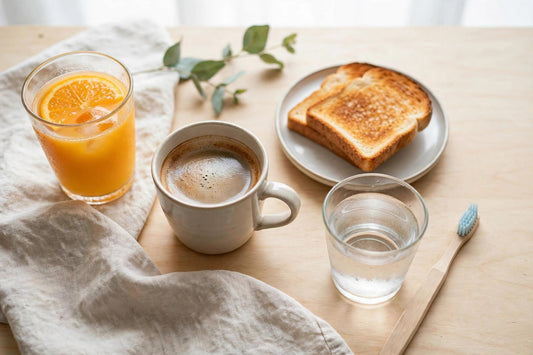 Person at a breakfast table with orange juice and coffee, toothbrush resting nearby next to a glass of water