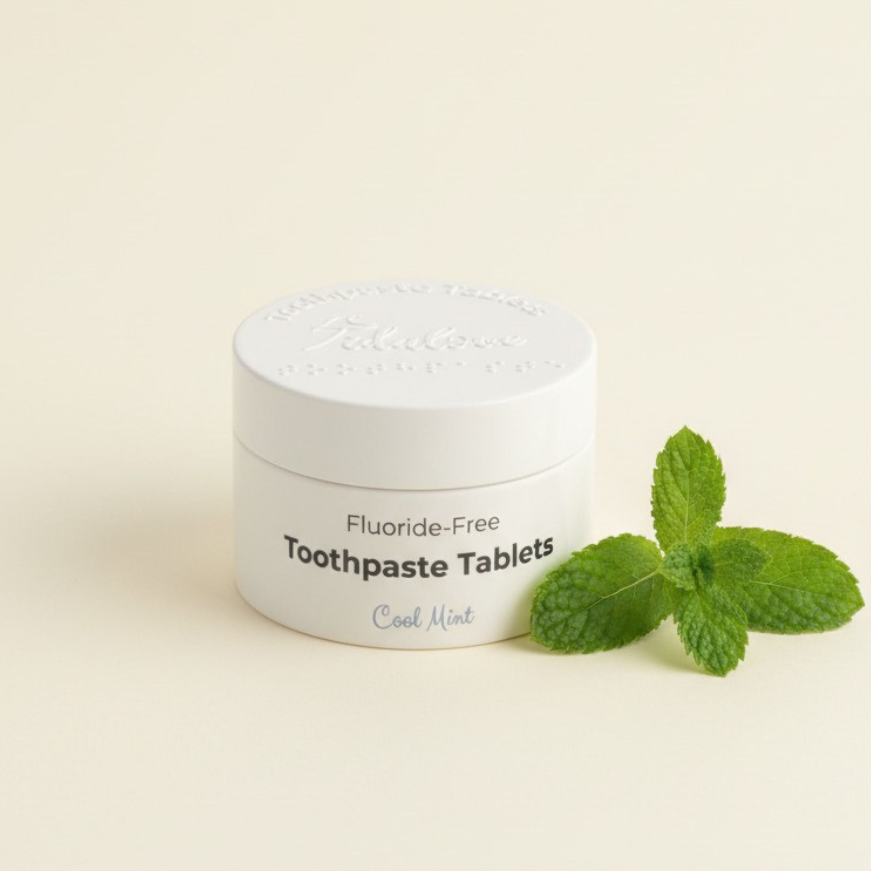 Jar of fluoride-free toothpaste tablets with a sprig of mint on a light background