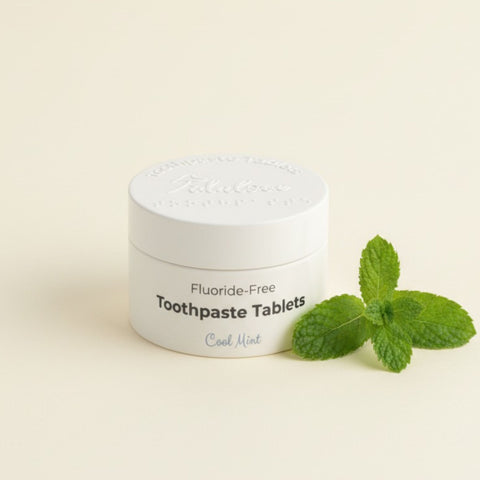 Jar of fluoride-free toothpaste tablets with a sprig of mint on a light background