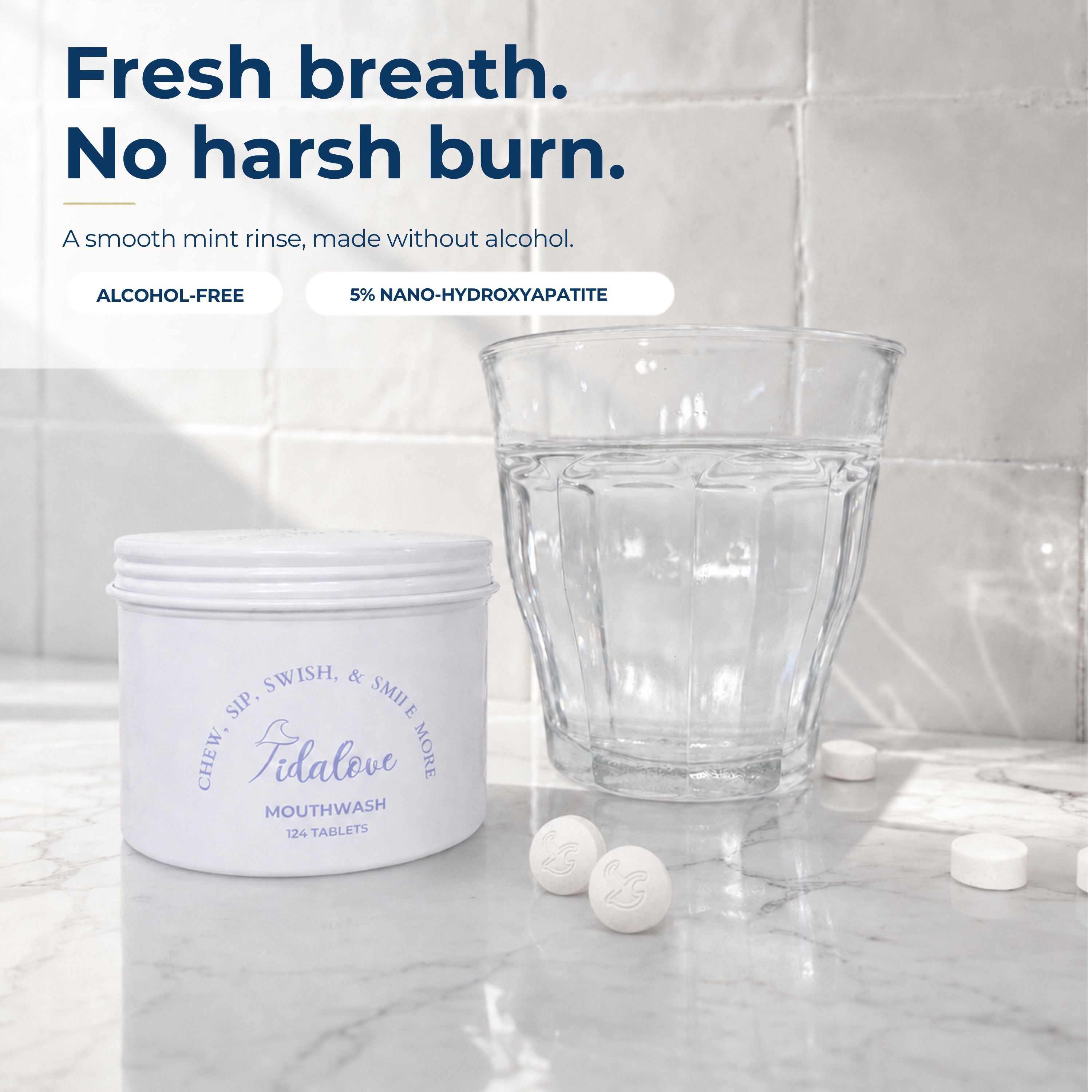 A white tub of Tidalove mouthwash with three tablets beside a clear glass on a marble surface against a tiled wall. Text at the top reads: 'Fresh breath.
