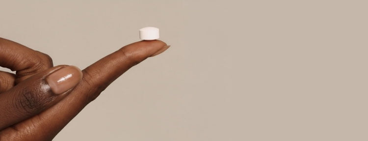 Hand holding a toothpaste tablet against a beige background